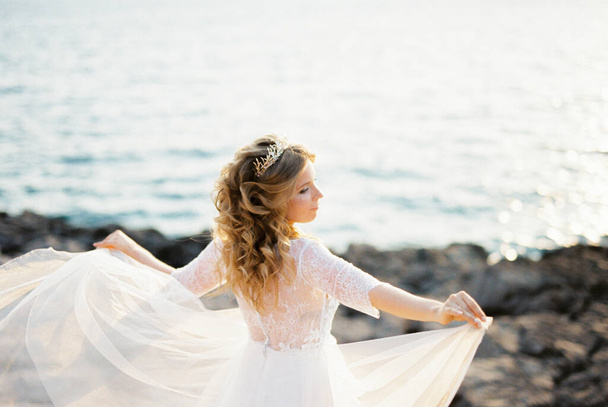 A menyasszony kinyújtott karokkal áll a ruhája szélén. Kiváló minőségű fénykép - Fotó, kép