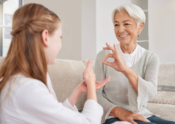 Senior woman, sign language and deaf girl communication, talking or conversation in home. Support, care and retired old female speaking to child with hearing disability in asl language hand gestures - Photo, Image