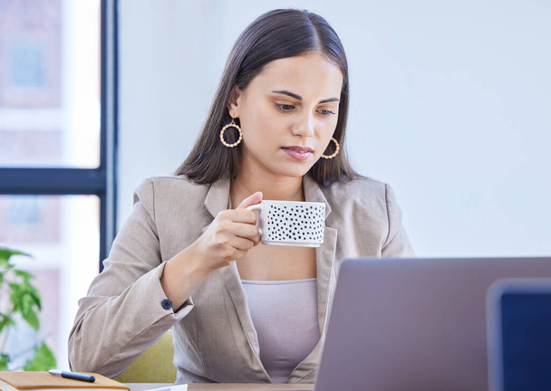 Habe meinen Kaffee repariert, jetzt können wir produktiv werden. eine junge Geschäftsfrau trinkt Kaffee, während sie in einem Büro an einem Laptop arbeitet - Foto, Bild