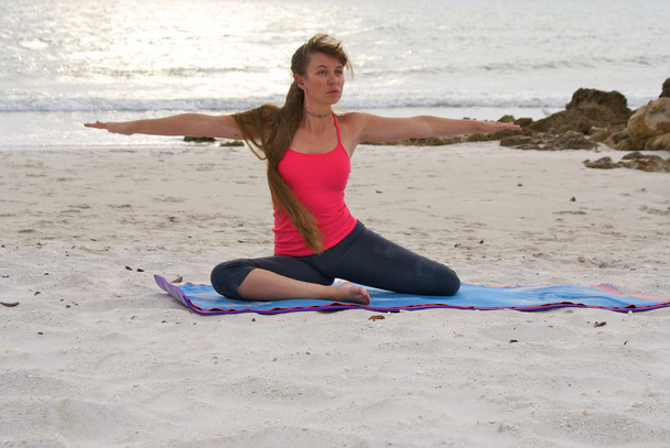 Mujer haciendo ejercicio de yoga sentada guerrera 2 pose en la playa al atardecer
 - Foto, imagen