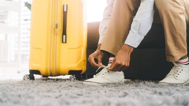 Азиатский турист вручную завязывает шнурки для начала путешествия с багажом. Люди, готовящиеся к праздникам, путешествуют. Фон с копировальным пространством. - Фото, изображение