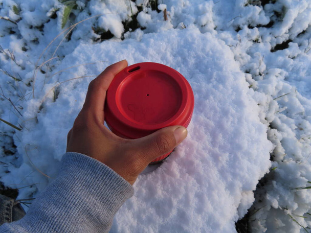 Persona con taza de café reutilizable en nieve pesada. - Foto, Imagen