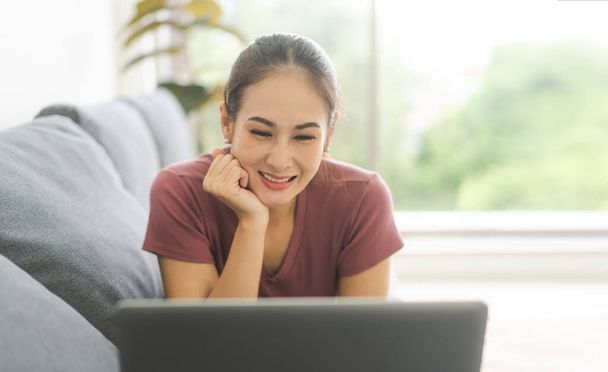 Junge erwachsene Südostasiatinnen bleiben zu Hause und arbeiten mit dem Laptop auf dem Sofa. Menschen leben mit Internet-Online-Technologie. Fensterlicht auf dem Hintergrund des Tages.  - Foto, Bild
