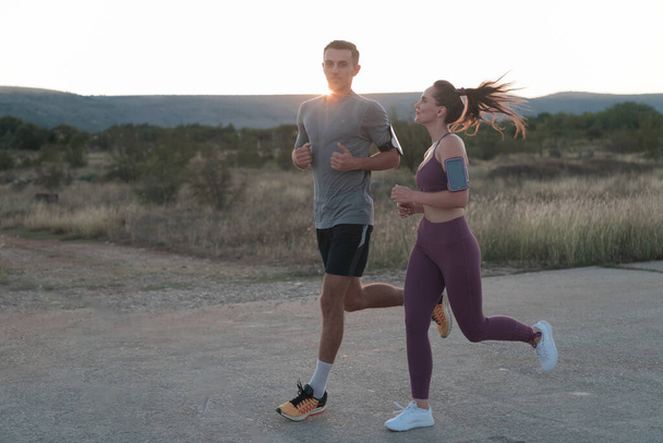 healthy young couple jogging in the city streets in the early morning with a beautiful sunrise in the background. High quality photo - Photo, Image