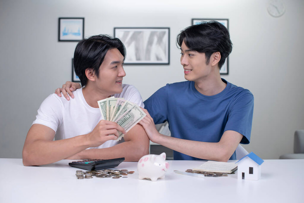 Young happy Asian gay couple saving money to buy a house. LGBT men couple saving money for family and home. - Photo, Image