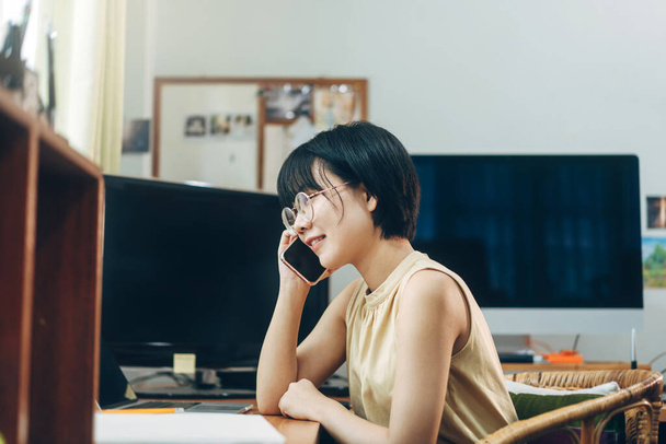 Mladá dospělá Asiatka zůstat a pracovat z konceptu domácí kanceláře. Obchodní žena používající chytrý telefon přes internet online. Pozadí s počítačem ve dne. - Fotografie, Obrázek