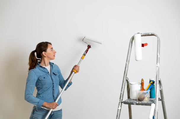 塗装ブラシやツールと壁、はしごを着色のためのペイントローラーを保持している女性。ホーム改善コンセプト. - 写真・画像