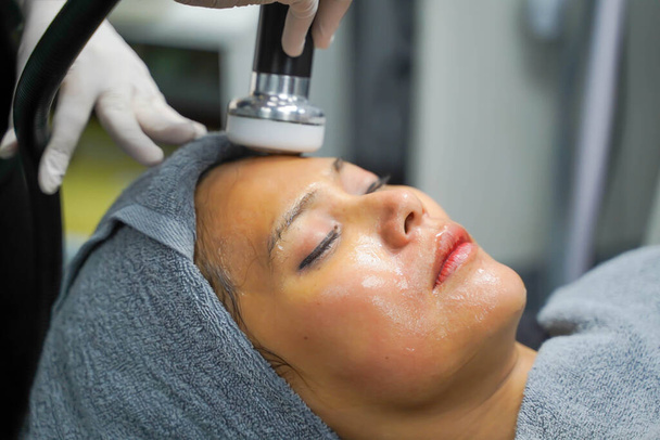 close-up aziatische schoonheid vrouw die therapie te stimuleren gezichtshuid en gezicht ultrasone huidverzorging behandeling door professionele cosmetoloog welzijn. - Foto, afbeelding
