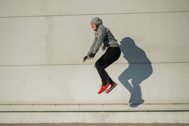 Caucasian man in hoodie jumping high with hands on knees outdoors - Fotó, kép