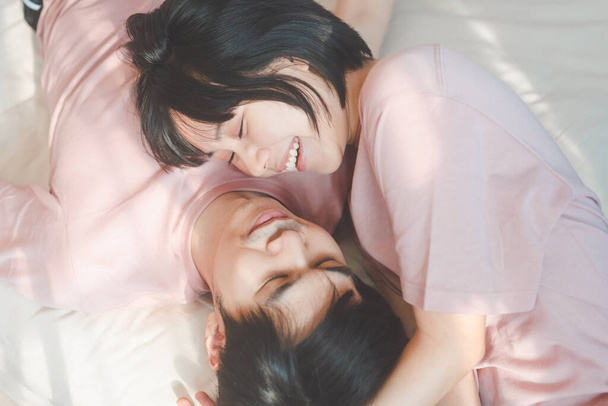 Junge erwachsene asiatische Liebhaberpaar zusammen leben zu Hause Konzept. Glücklich lächelnde Menschen im Schlafzimmer tragen rosa Hemd. - Foto, Bild