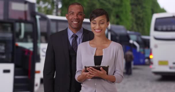 Dois jovens agentes de viagens africanos posando juntos lá fora perto de alguns ônibus turísticos. Feliz confiante profissional de aparência preto macho e fêmea olhando para a câmera. 4k - Filmagem, Vídeo