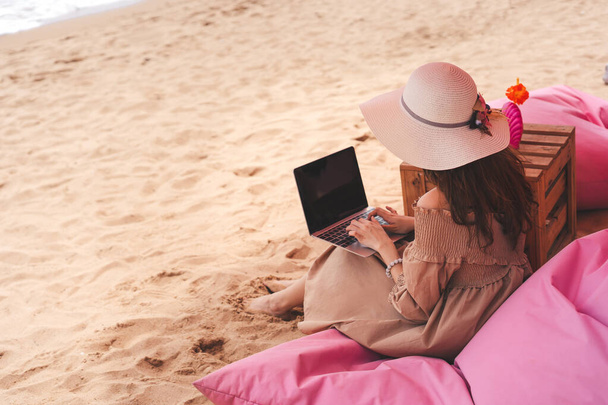 Concetto di lavoro e viaggi d'affari. Vista posteriore della giovane donna asiatica del sud-est asiatico che utilizza il computer portatile presso la spiaggia di sabbia rosa caffè di lusso sul mare. Stile di vita freelance in vacanza. - Foto, immagini