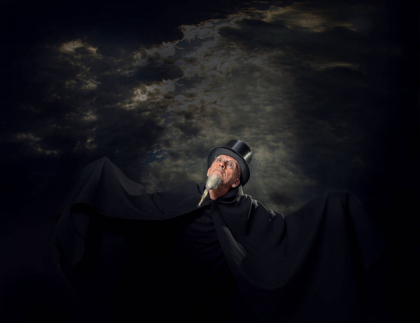 Πορτρέτο ενός μυστηριώδους αρσενικού μάγου με μαύρο ψηλό καπέλο και μαύρη ρόμπα. - Φωτογραφία, εικόνα