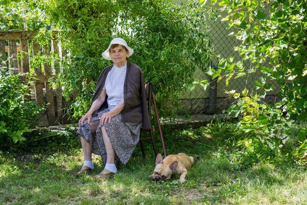 Portrait of an elderly woman in a white panama against a background of green foliage. - Φωτογραφία, εικόνα