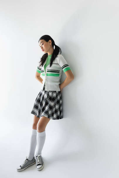 Young asian woman in sneakers and skirt standing on grey background  - Photo, Image