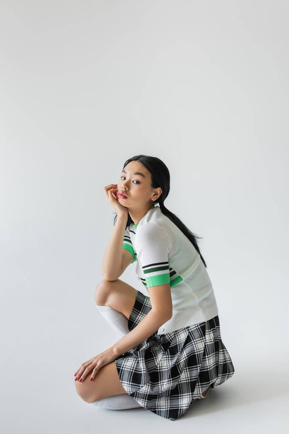 Young asian woman in checkered skirt and knee socks posing on grey background  - Foto, imagen