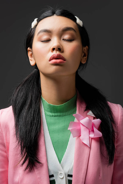 Portrait of stylish asian model in jacket closing eyes isolated on grey  - Foto, imagen