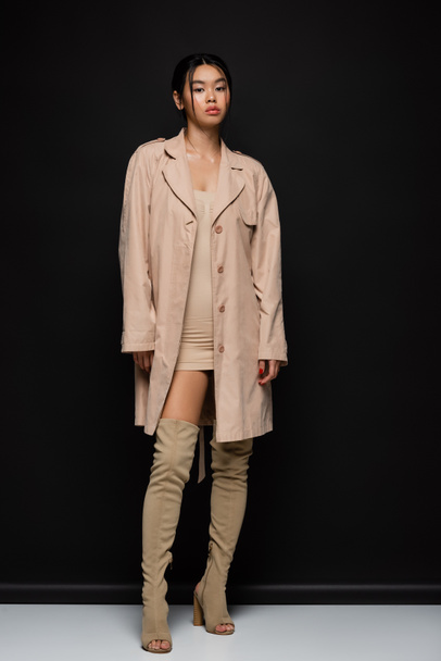 Stylish asian woman in trench coat and boots standing on black background  - Φωτογραφία, εικόνα