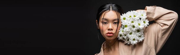 Tyylikäs aasialainen nainen trenssi takki tilalla krysanteemit lähellä kasvot eristetty musta, banneri  - Valokuva, kuva