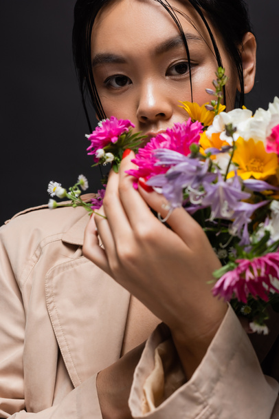 黒で隔離されたぼやけた花を保持ベージュトレンチコートのスタイリッシュなアジアモデル  - 写真・画像