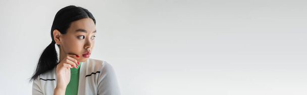 Hezký asijský model v svetru odvrací pohled izolované na šedé s kopírovacím prostorem, banner  - Fotografie, Obrázek