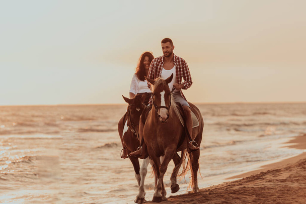 A loving couple in summer clothes riding a horse on a sandy beach at sunset. Sea and sunset in the background. Selective focus. High quality photo - Fotoğraf, Görsel
