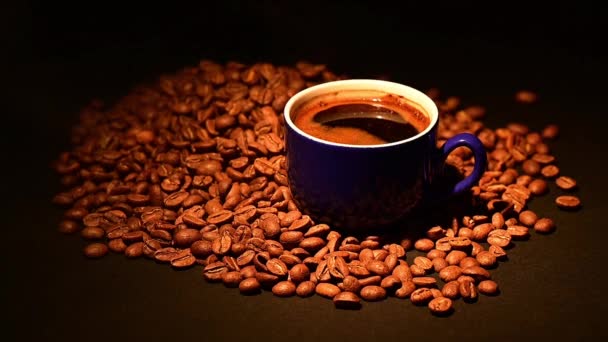 Una taza de café en granos de café, café iluminado por la luz cálida, café sobre un fondo negro, video en cámara lenta y video hd. - Imágenes, Vídeo