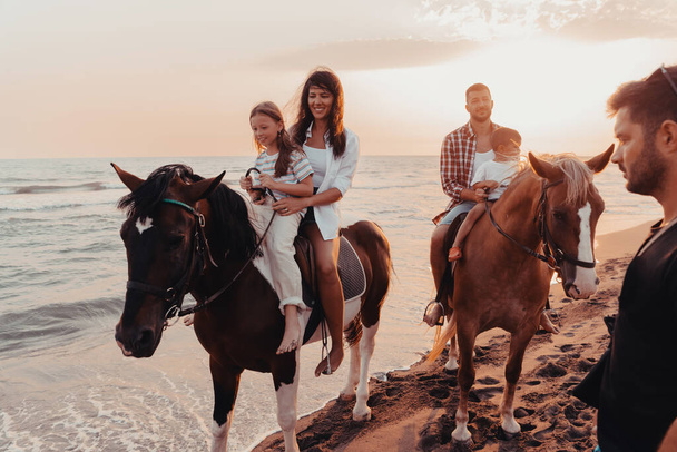 The family spends time with their children while riding horses together on a sandy beach. Selective focus. High quality photo - Фото, изображение