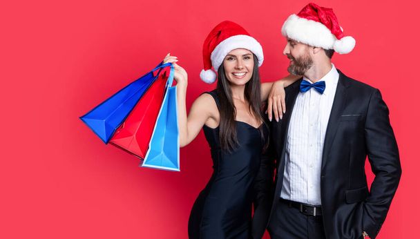 xmas couple on shopping isolated on red background, copy space. xmas shopping bags and couple. merry xmas to couple with shopping bags in studio. shopping couple at xmas sale. - 写真・画像