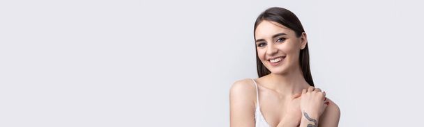 Mulher sorridente bonita com pele limpa, maquiagem natural e dentes brancos em um fundo cinza - Foto, Imagem