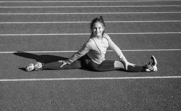 Flexible girl child in sportswear do splits on athletics track, stretching. - Fotografie, Obrázek