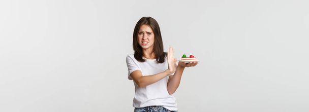 Walgelijke jonge vrouw verwerpt het eten van vreselijke taart, maakt weigering gebaar en grimmig ontevreden. - Foto, afbeelding