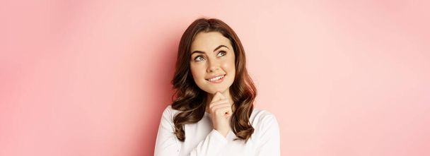 Close up portrait of coquettish smiling woman, glamour girl thinking, looking thoughtful, standing over pink background. - Photo, Image