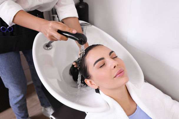 Professional hairdresser washing woman's hair in beauty salon, closeup - Photo, image