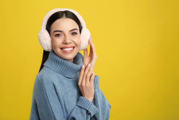 Beautiful young woman wearing earmuffs on yellow background. Space for text - Fotoğraf, Görsel