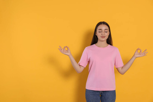 Find zen. Beautiful young woman meditating on yellow background. Space for text - Фото, изображение