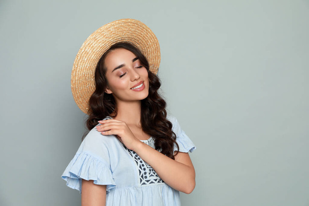 Beautiful young woman with straw hat on light grey background. Space for text - Foto, afbeelding