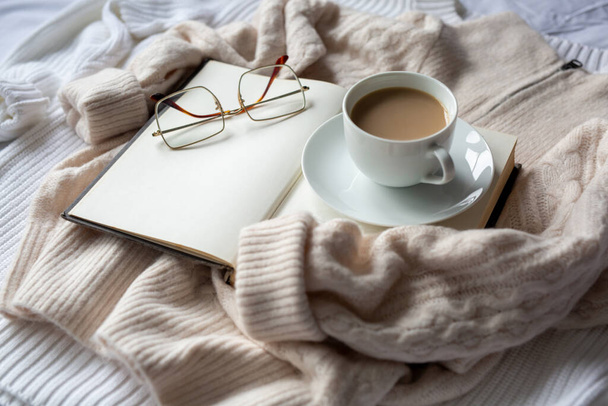 Open bruin boek met blanco pagina 's en mok cacao met schotel op warme beige trui, vierkante glazen. Herfst stemming, hygge en comfort - Foto, afbeelding