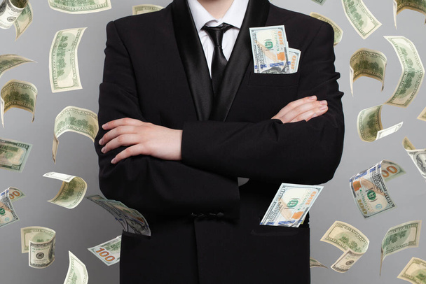 Бизнесмен стоит под денежным дождем, изолированным на сером фоне - Фото, изображение