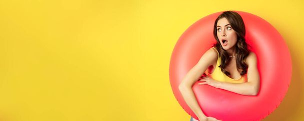 Primer plano retrato de mujer sexy joven coqueta dentro de anillo de natación rosa, concepto de vacaciones en la playa, vacaciones y verano, fondo amarillo. - Foto, imagen