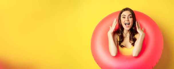 Красива курйозна жінка всередині рожевого плавального кільця, позує на літні канікули, концепція пляжного відпочинку, що стоїть на жовтому тлі
. - Фото, зображення