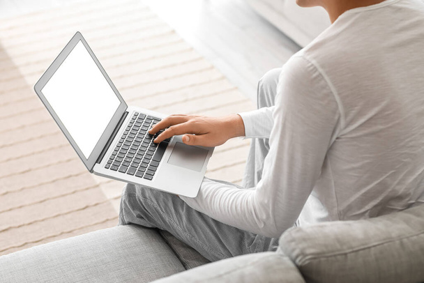 Молодий чоловік використовує ноутбук на дивані вдома, крупним планом
 - Фото, зображення