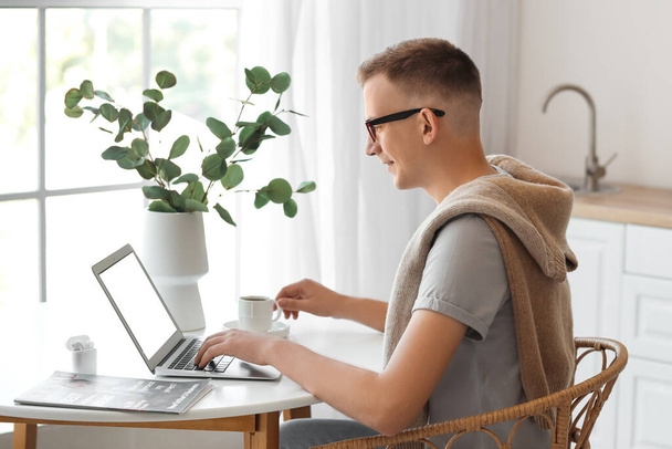 Nuori mies, jolla on kuppi kahvia kannettavan tietokoneen avulla toimistossa - Valokuva, kuva