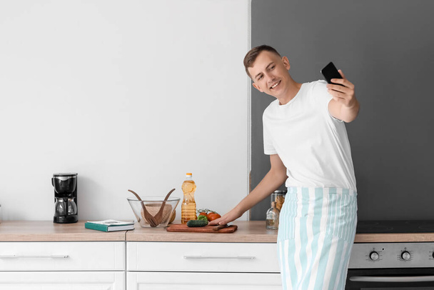 Mladý muž s mobilním telefonem s selfie v kuchyni - Fotografie, Obrázek