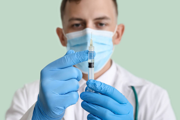 Male doctor in medical mask with syringe on green background, closeup - Foto, afbeelding