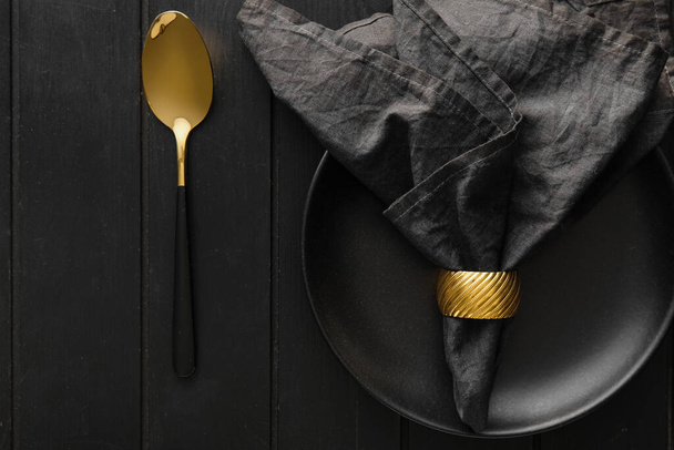 Stylish table setting with napkin in plate and cutlery on black wooden background - Photo, Image