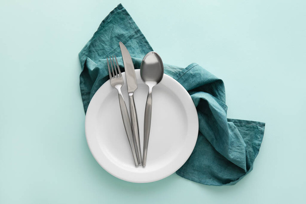 Simple table setting with cutlery in plate and green napkin on color background - Photo, Image