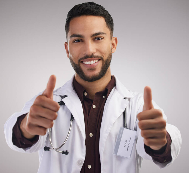 Sei in buone mani. un bel giovane medico in piedi da solo in studio e facendo un gesto pollice in alto mano - Foto, immagini