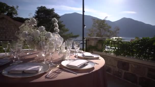 Szolgált ünnepi asztal virágokkal áll a teraszon a háttérben a hegyek. Kiváló minőségű FullHD felvételek - Felvétel, videó