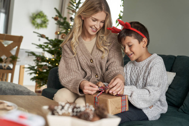 Caucásico chico y madre embalaje regalo de Navidad en sofá  - Foto, imagen